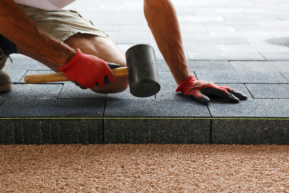 Hands of a Worker Laying Paving, Big Concrete Paver Blocks, in Motion With Hammer in Hand.