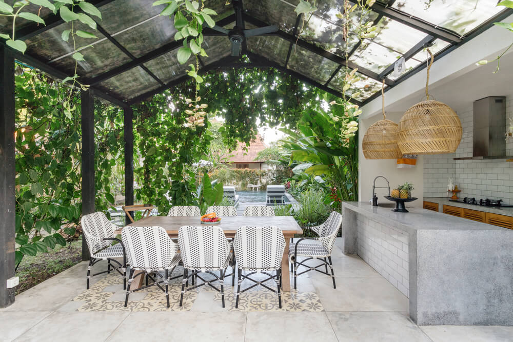 Open Kitchen With Empty Dining Room Table and Chairs Outside, Against Green Fresh Plants on Background