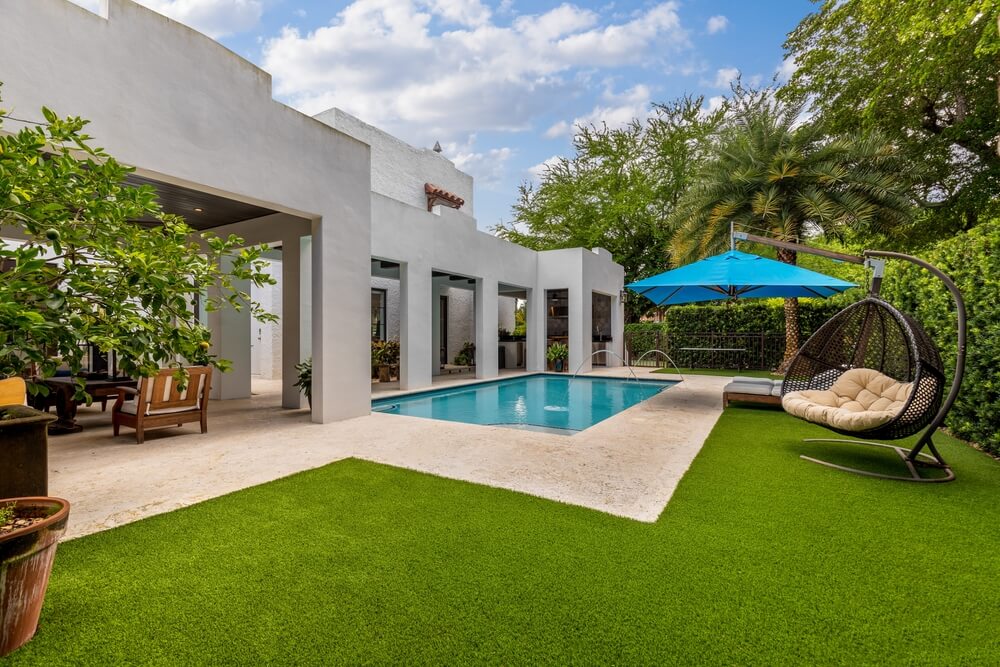 Backyard of a Modern House With Swimming Pool, Artificial Grass, Trees, Chairs and an Umbrella