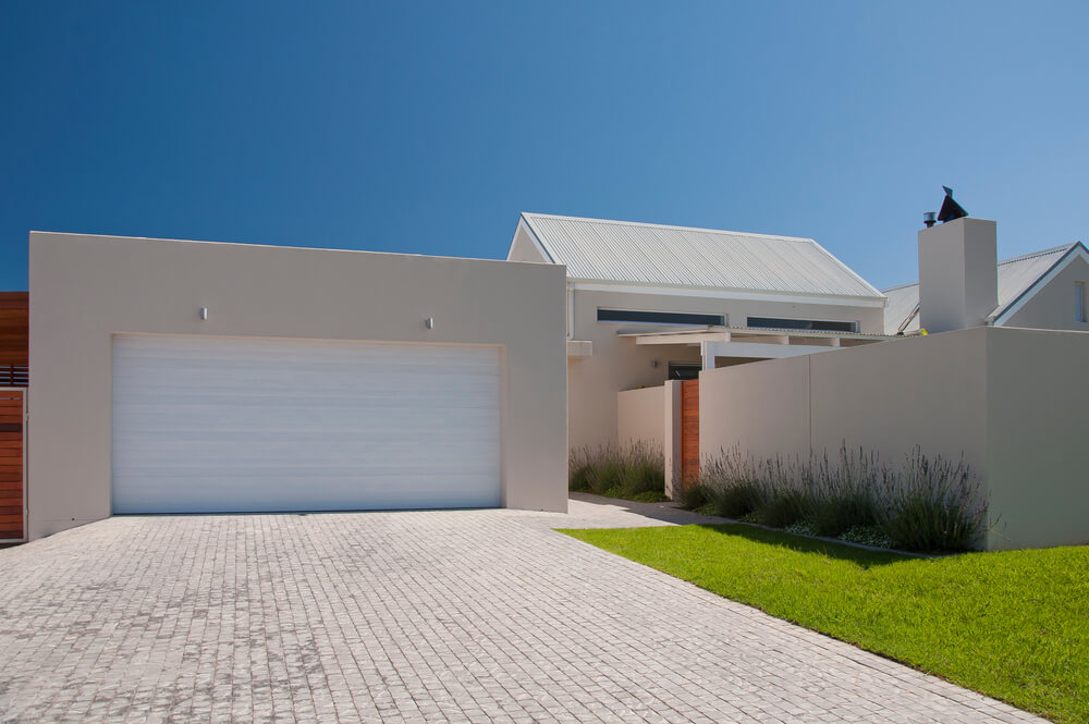 Facade of a Modern House From the Street With White Walls, Lavender Plants, Green Lawn and Garage Driveway