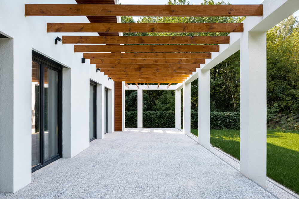 Elegant Home Patio With Stone Floor and Wooden Elements on Ceiling and Green Grass Backyard