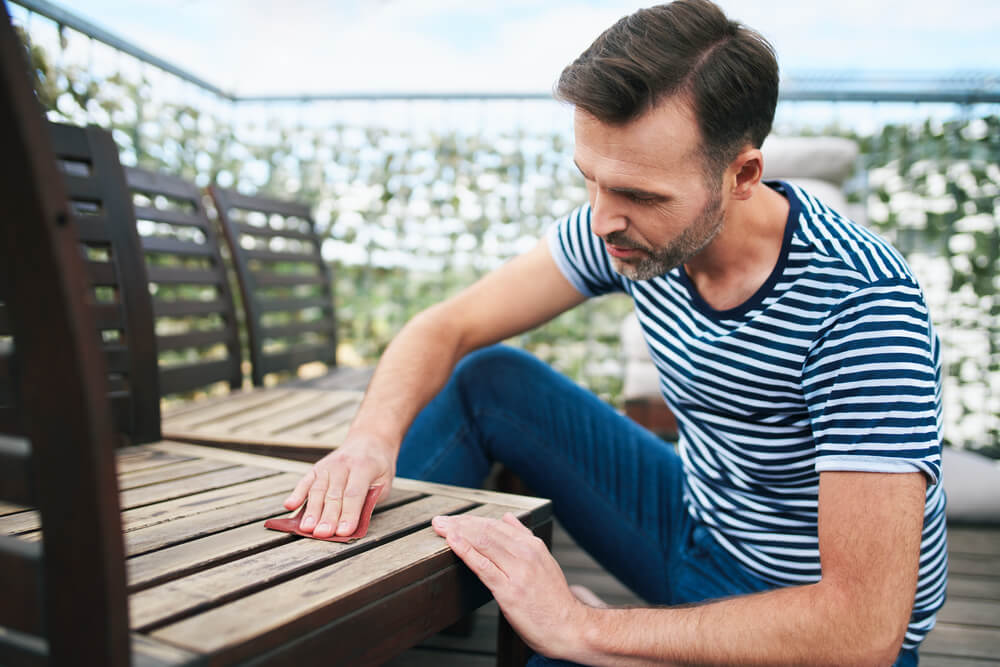 Handsome Man Sitting on Apartment Terrace and Sanding Wooden Garden Chairs.